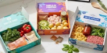 Three different meal kit boxes open on a kitchen counter, showcasing fresh ingredients and recipe cards.